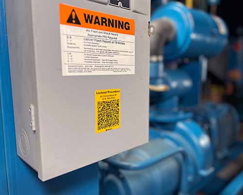 A breaker box inside a maufacturing facility. It has bright warning labels on it.