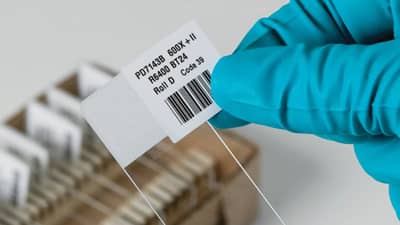 A lab technician holding a slide with a white barcode label.
