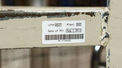 A Brady ultra aggressive adhesive label applied to the battered edge of a warehouse shelf.