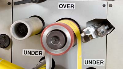 Several Brady all-weather vinyl labels with the text OVER and UNDER applied to a die-cut machine to indicate the direction material should be threaded.