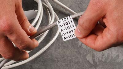 A Brady repositionable nylon cloth label with the text A-1011 printed on it multiple times being applied to a gray cable.